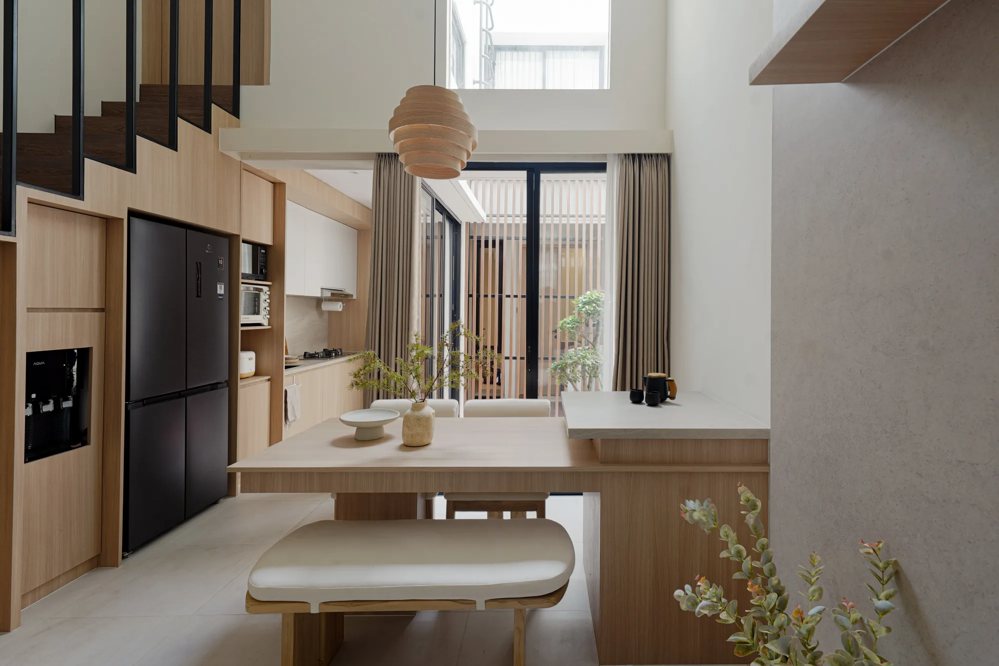 Open kitchen and dining area beneath the double-height void, lit by a timber pendant and courtyard glazing.