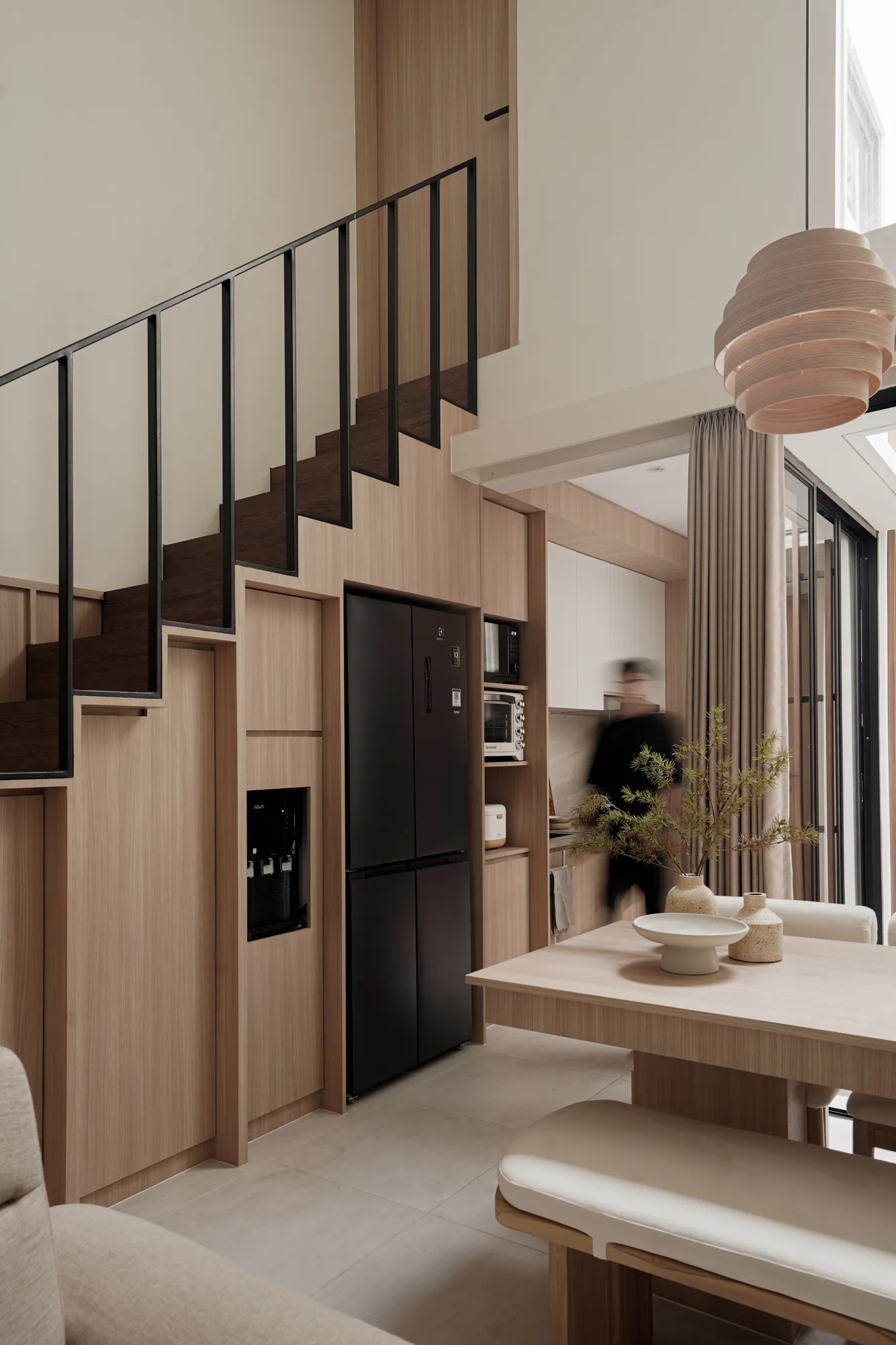 Dark timber stair rising above integrated storage and a compact kitchen, with a blurred figure in motion.