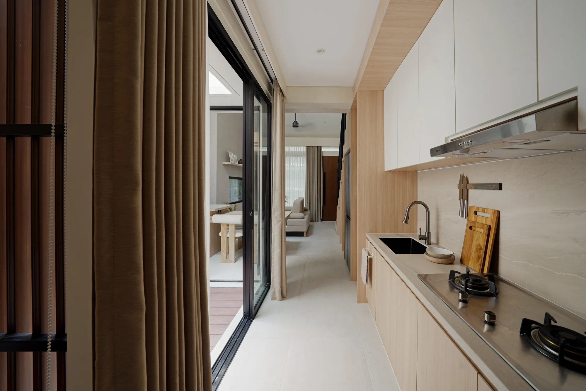 Narrow galley kitchen with pale cabinets, stone-look counter and sliding glass doors opening toward the courtyard.