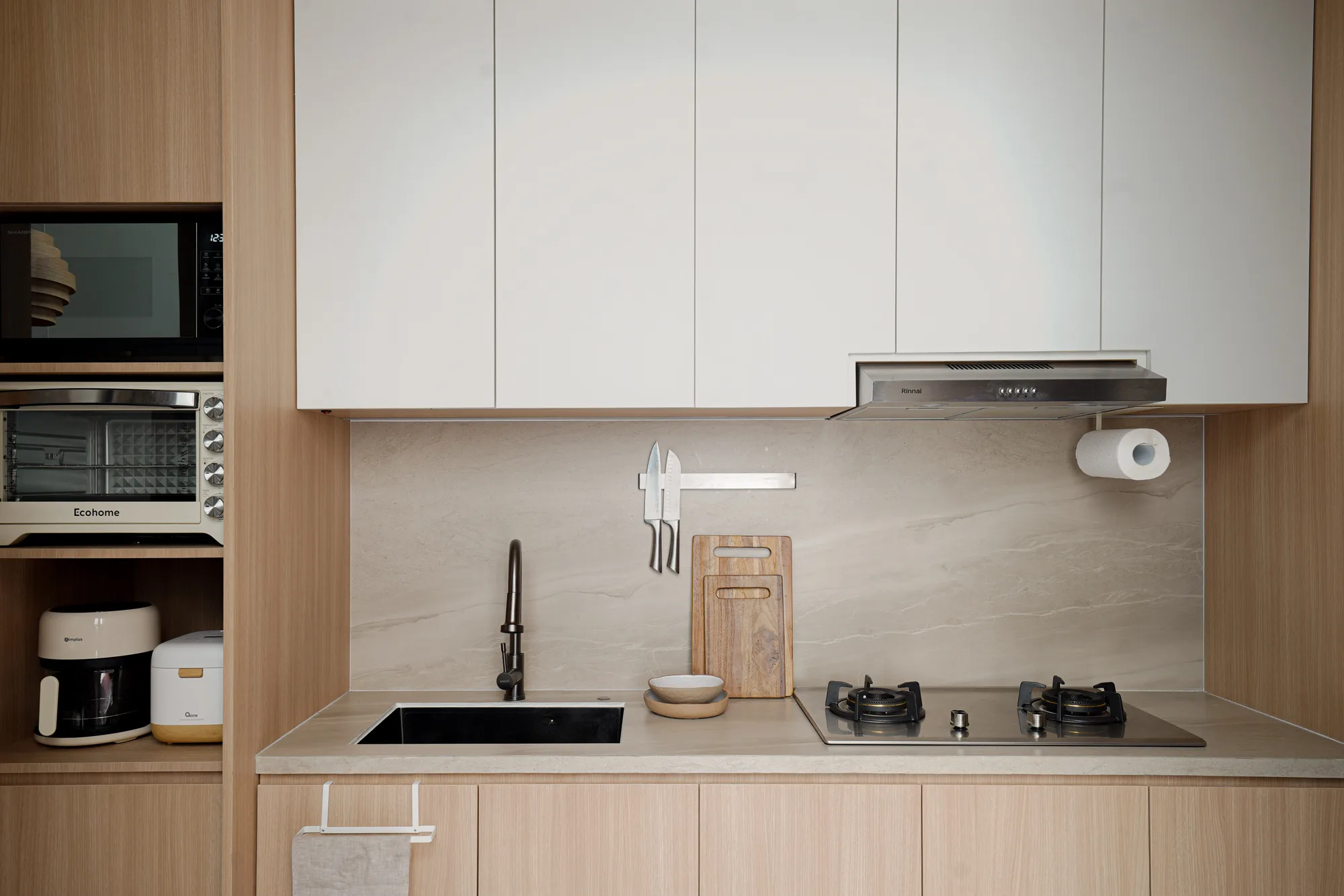 Compact kitchen counter with a black sink, gas cooktop, timber cutting boards and wall-mounted knives.