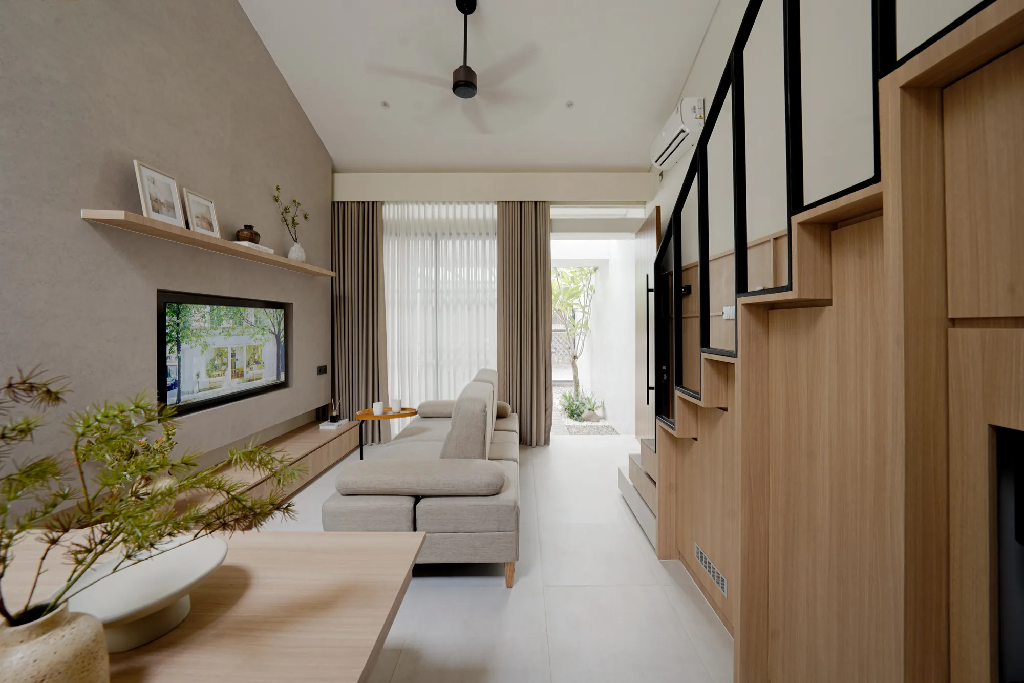 Living room with pale sofa, timber media wall and black steel stair, opening onto the planted courtyard.