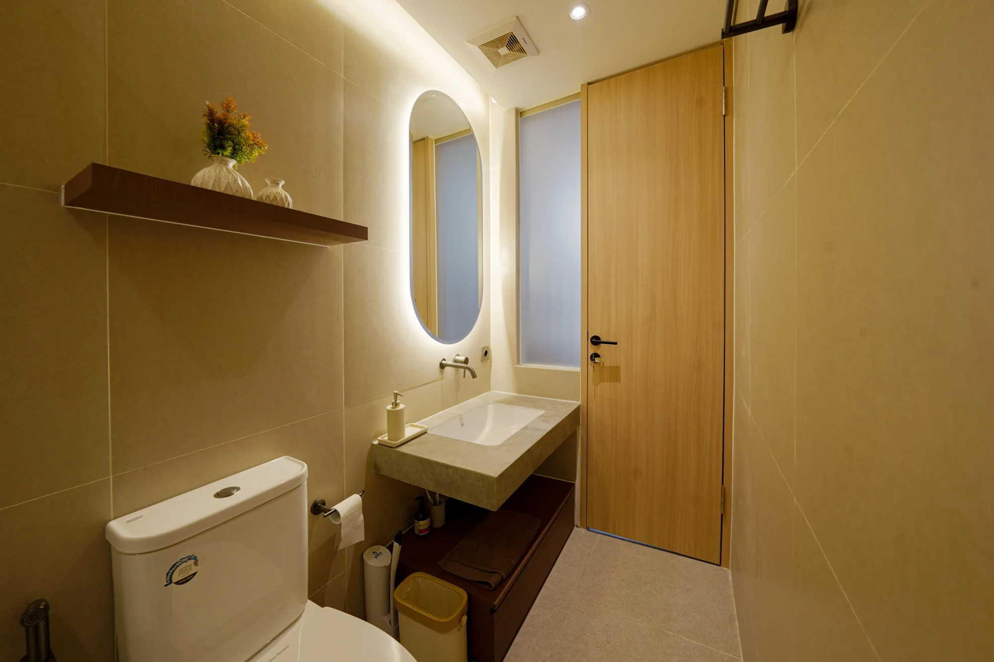 Warmly lit bathroom with a floating stone vanity, arched mirror and frosted glass door.