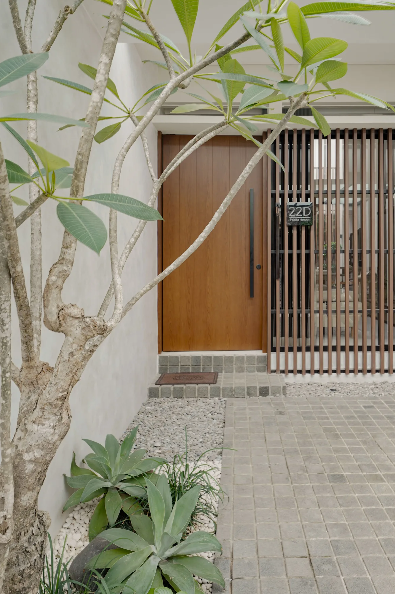 Frangipani tree and low planting framing Prada House's timber front door and vertical entry screen.