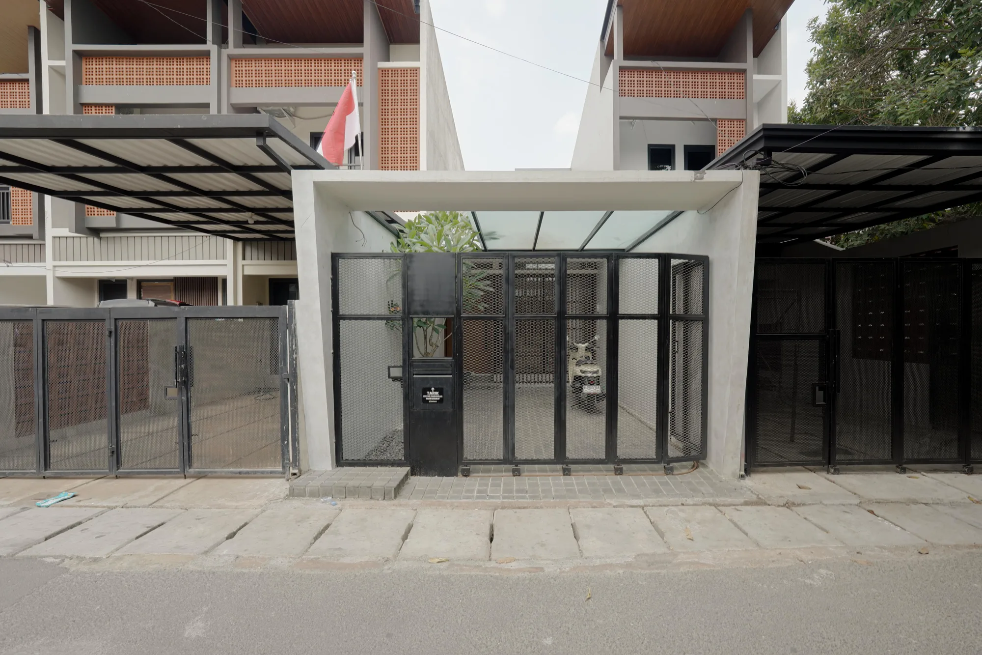 Front elevation of Prada House with a perforated steel gate, glass carport roof and a frangipani tree behind it.