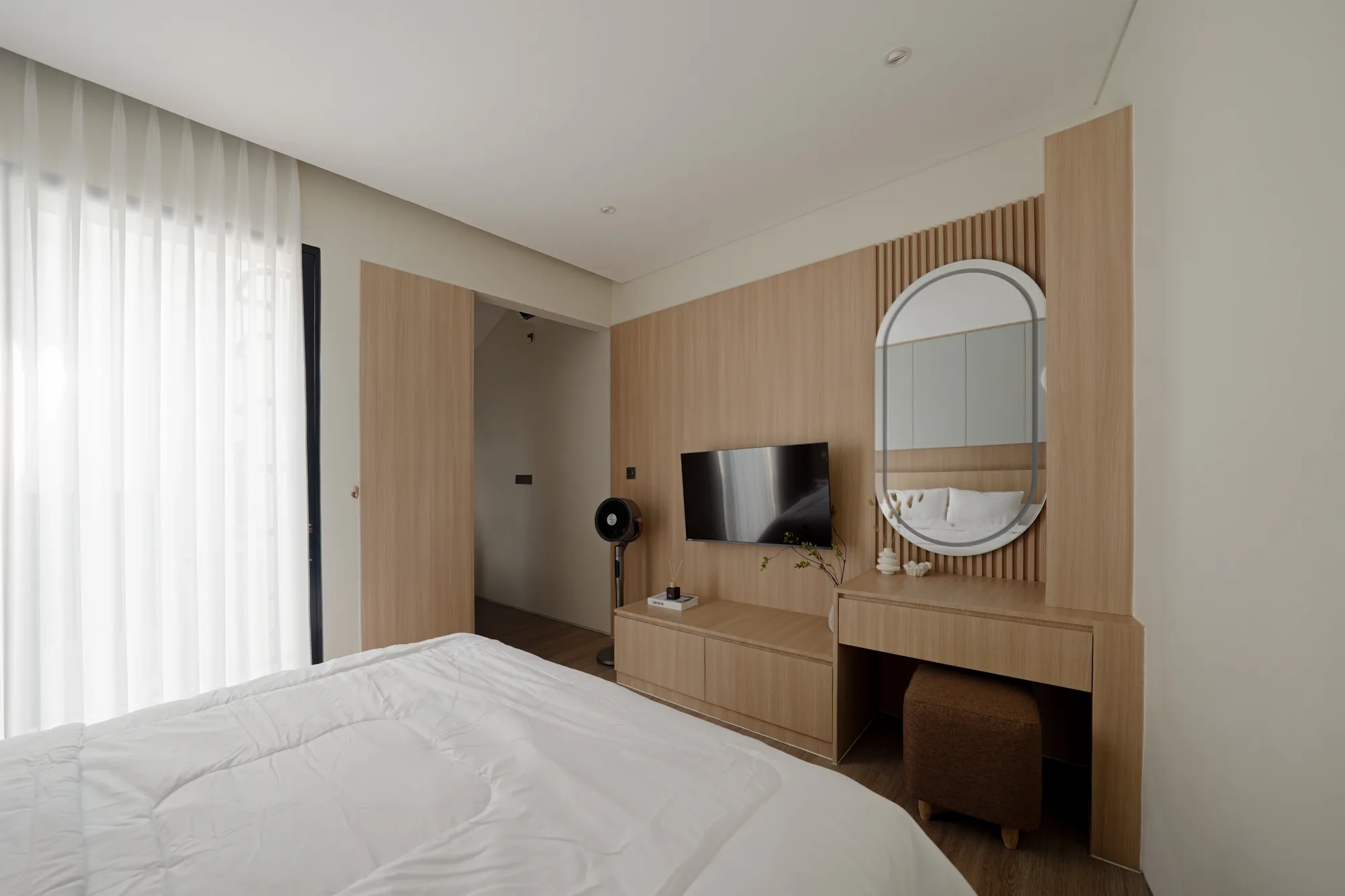 Bedroom media wall in pale timber, with an oval mirror above a compact dressing desk.