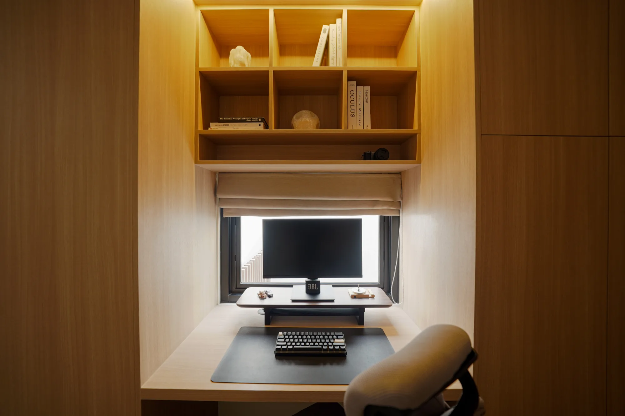 Backlit timber study nook with open shelves, a desk monitor and a black task chair.