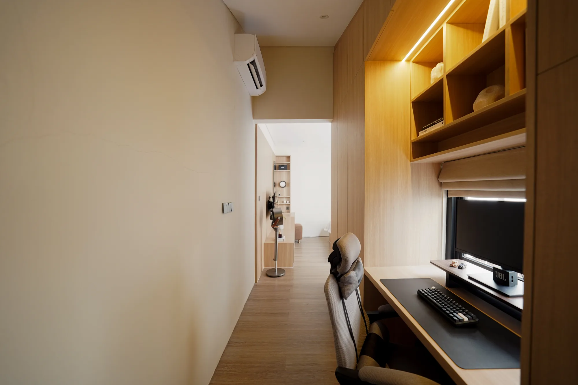 Study corridor with a backlit timber shelf, desk monitor and a view toward the bedroom beyond.