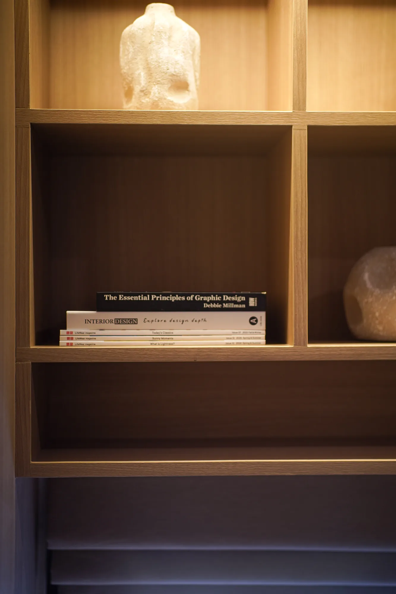 Close view of a backlit timber display shelf with books and small sculptural objects.