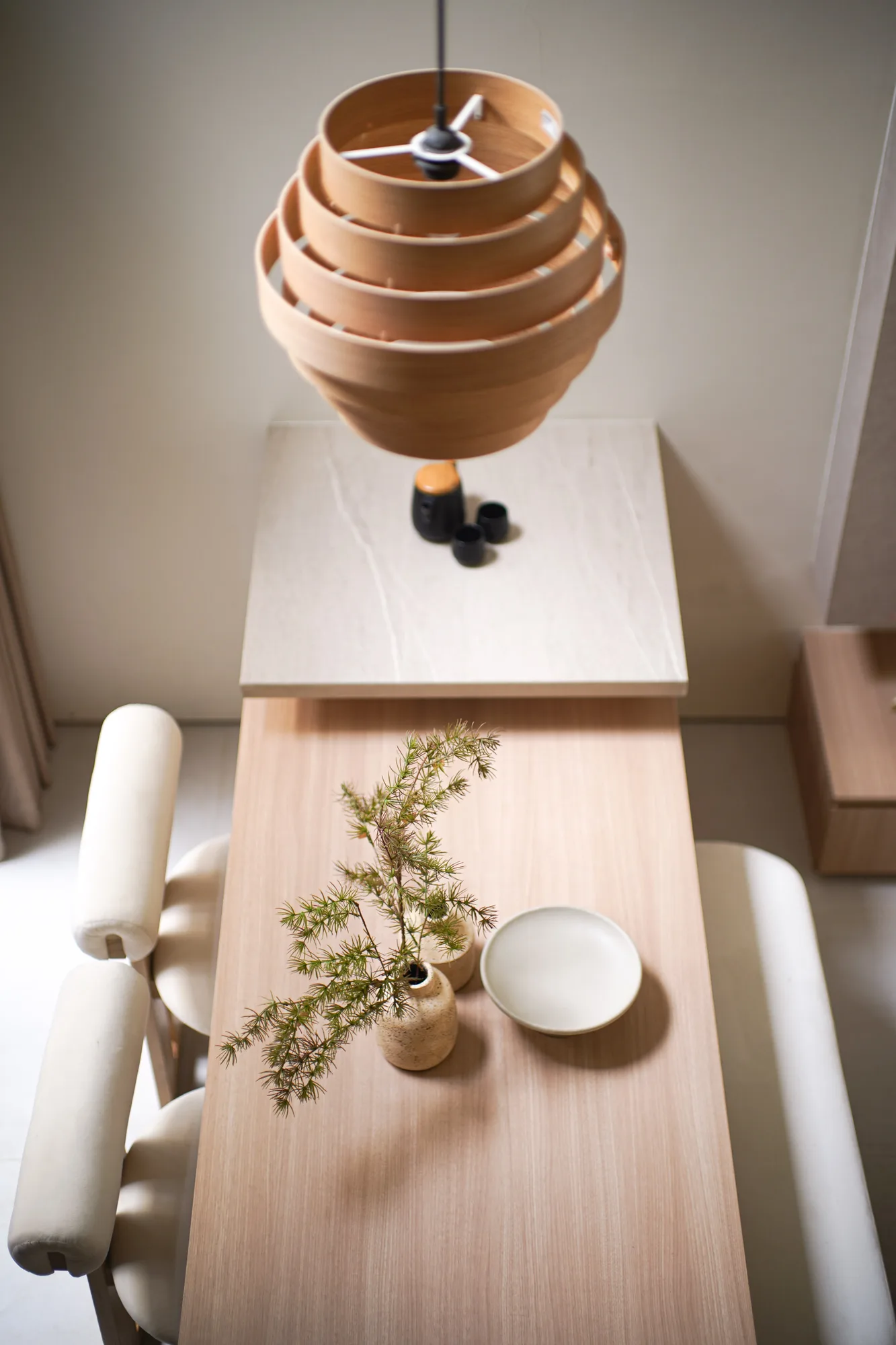 Layered timber pendant light suspended over a pale stone-look counter and dining table.