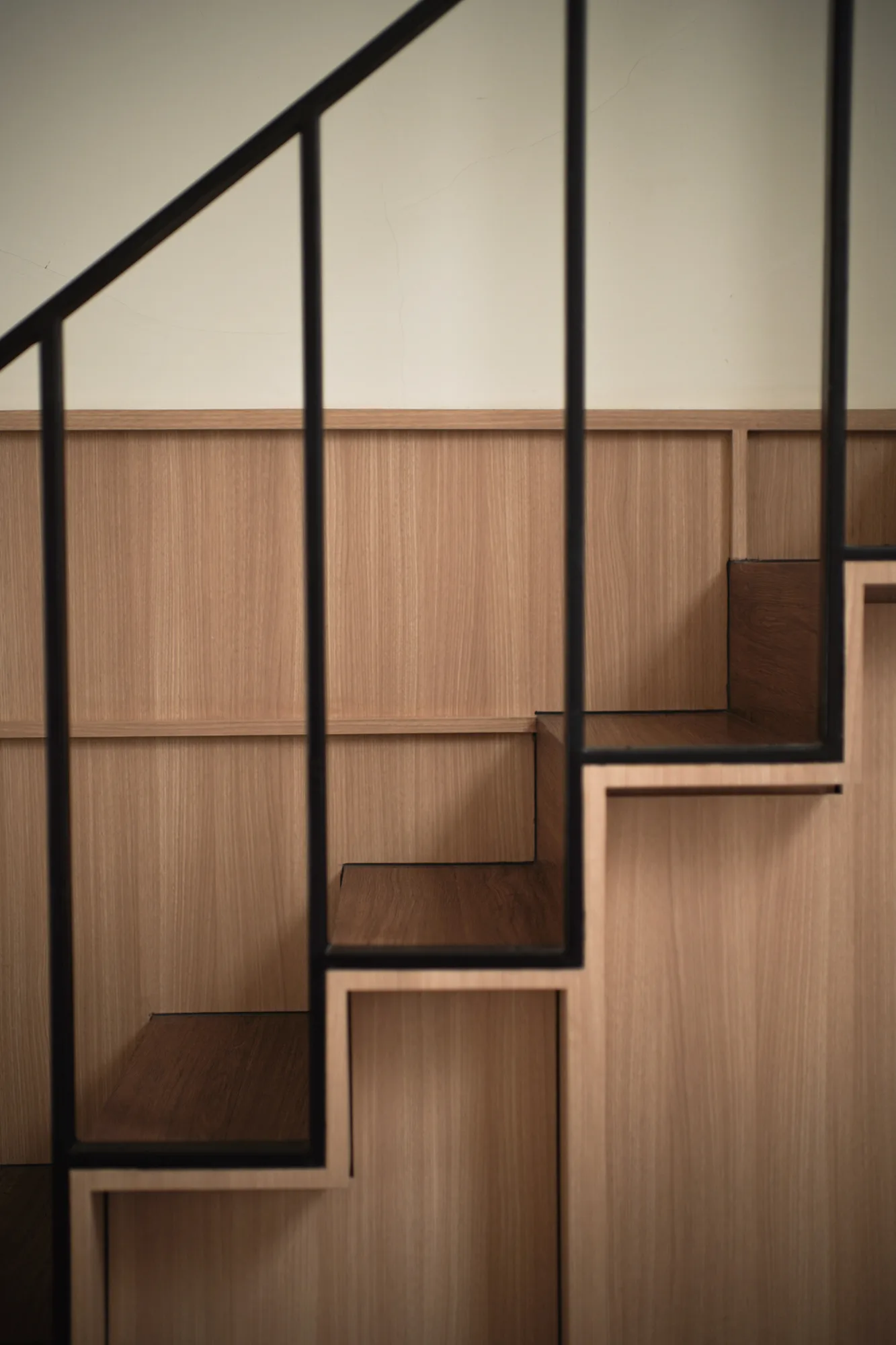 Black steel stair railing set against pale timber wall panelling and dark timber treads.
