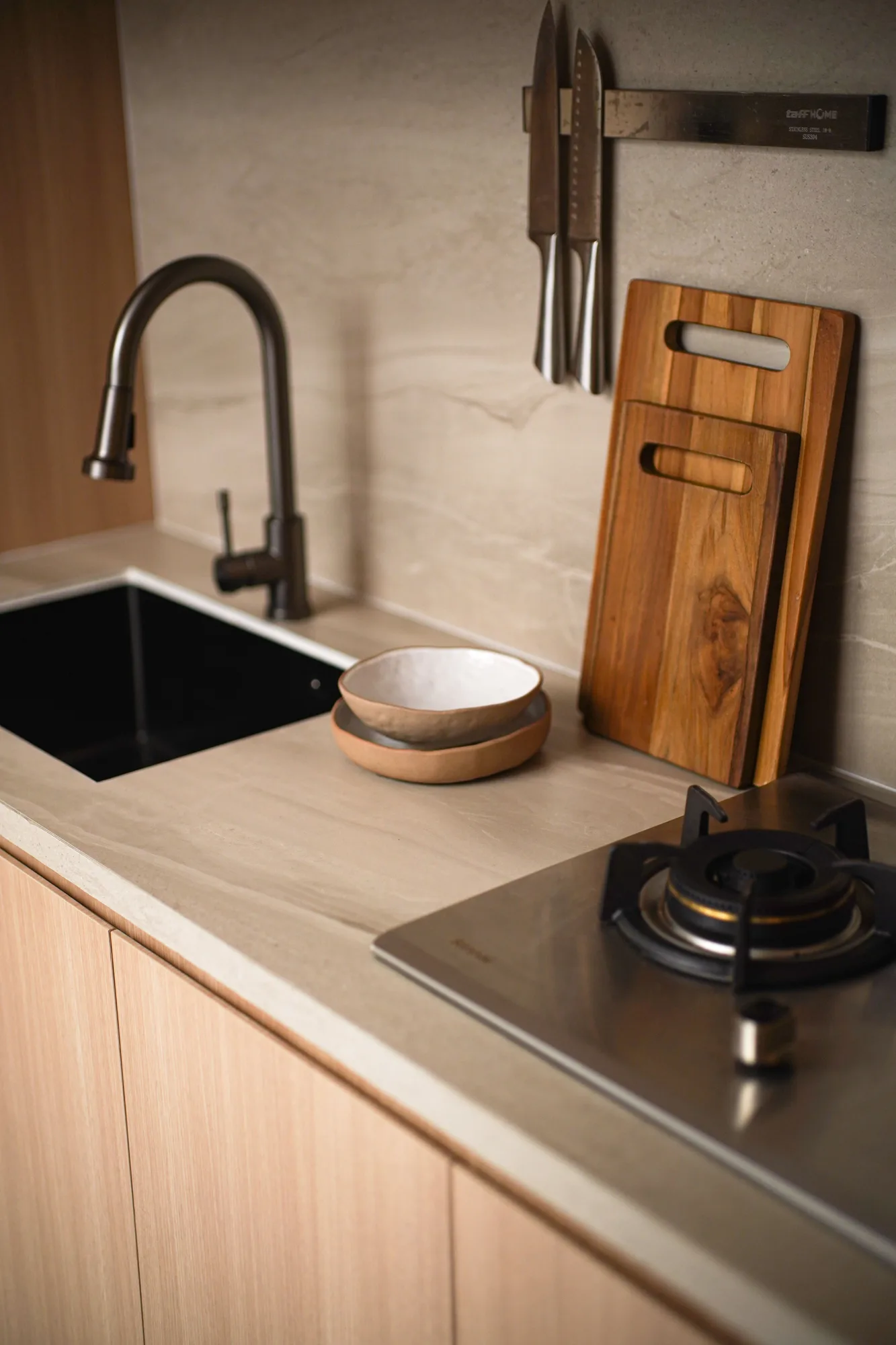 Kitchen close-up with black tap, stone-look counter, timber cutting boards and a gas cooktop.
