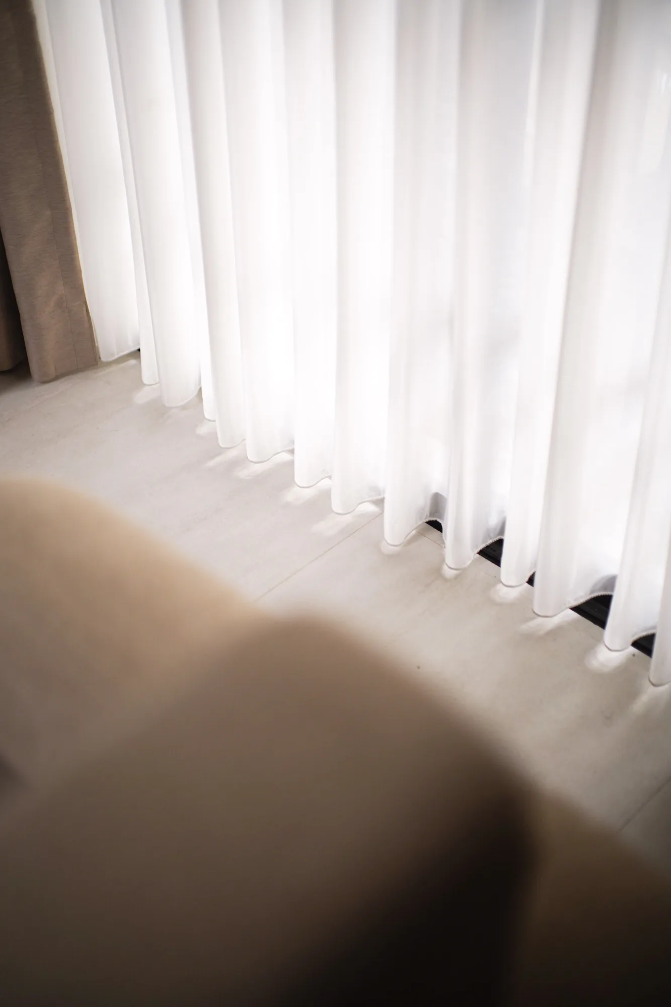 Sheer white curtains pooling softly above the pale tiled floor.