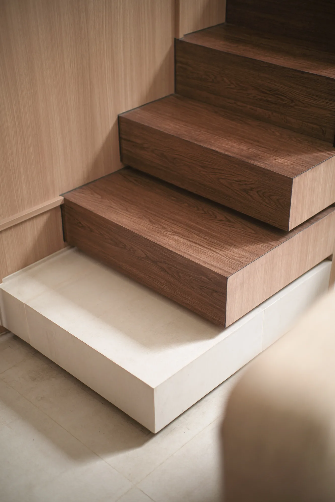 Dark timber stair treads meeting pale timber panelling and a light tiled floor.