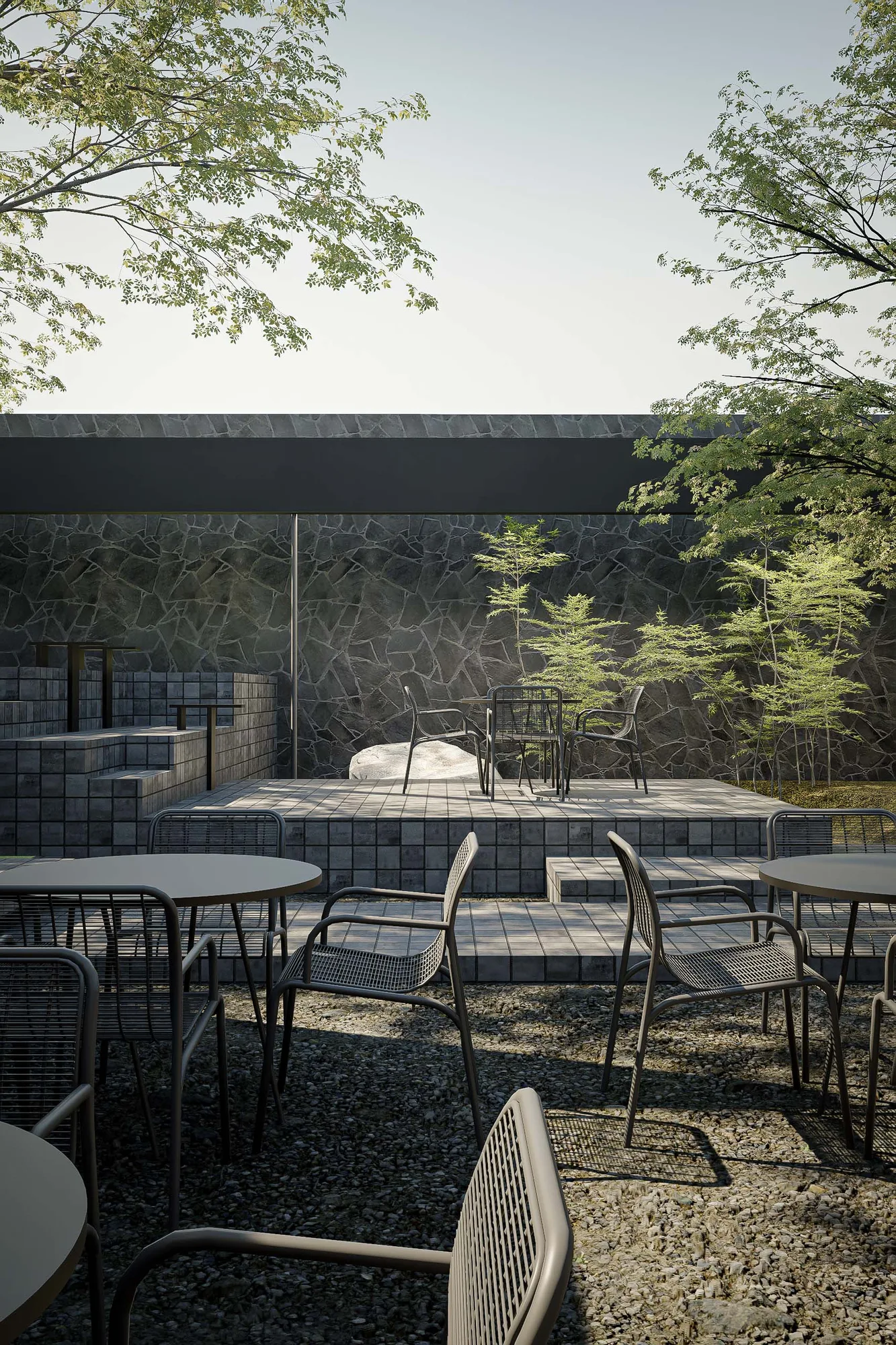The same garden corner seen from the courtyard tables, stone wall and young trees enclosing the seating beyond.
