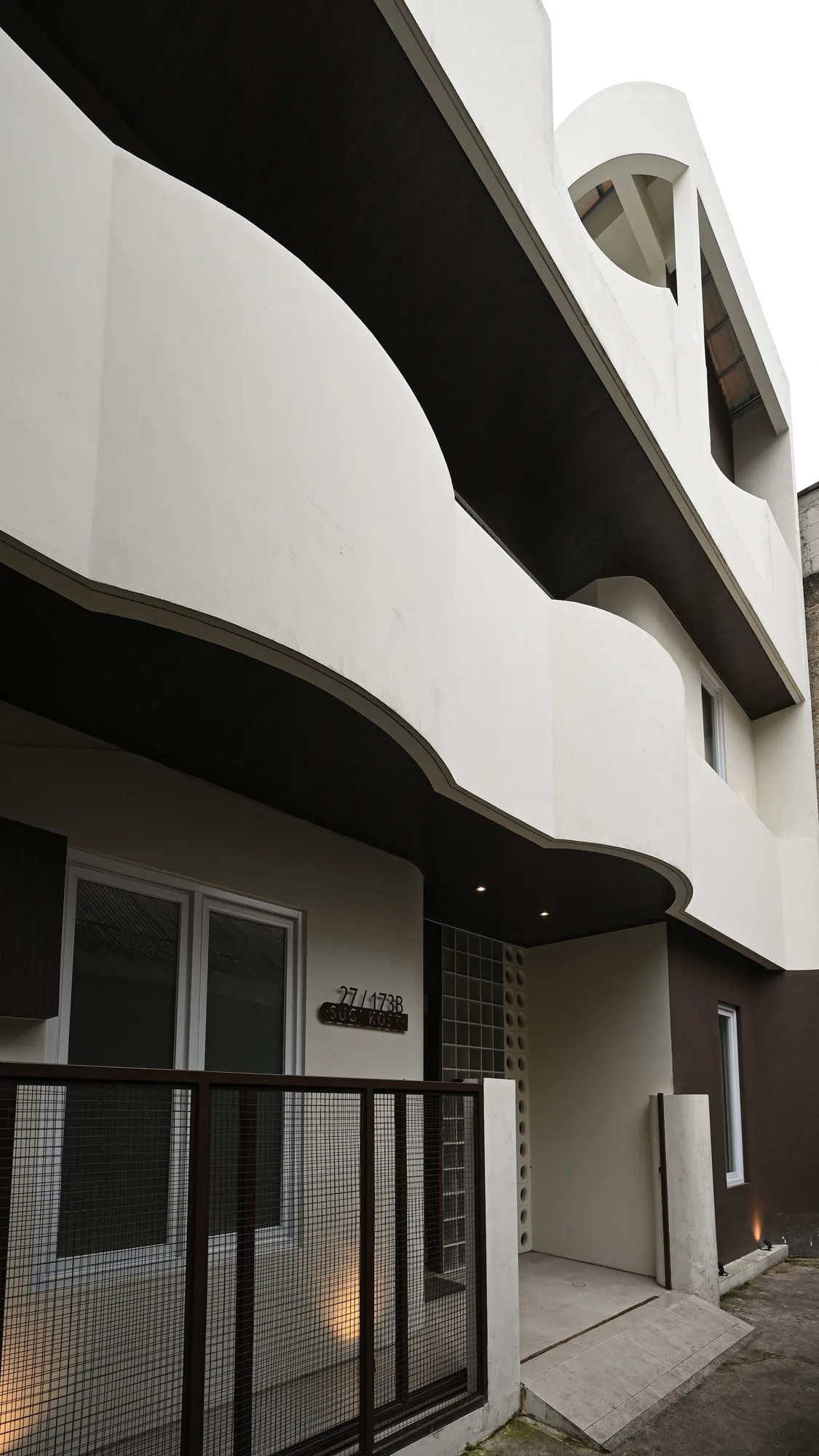 Looking up at the building's curved white upper floors, where dark soffits step back above the glass-block entrance.