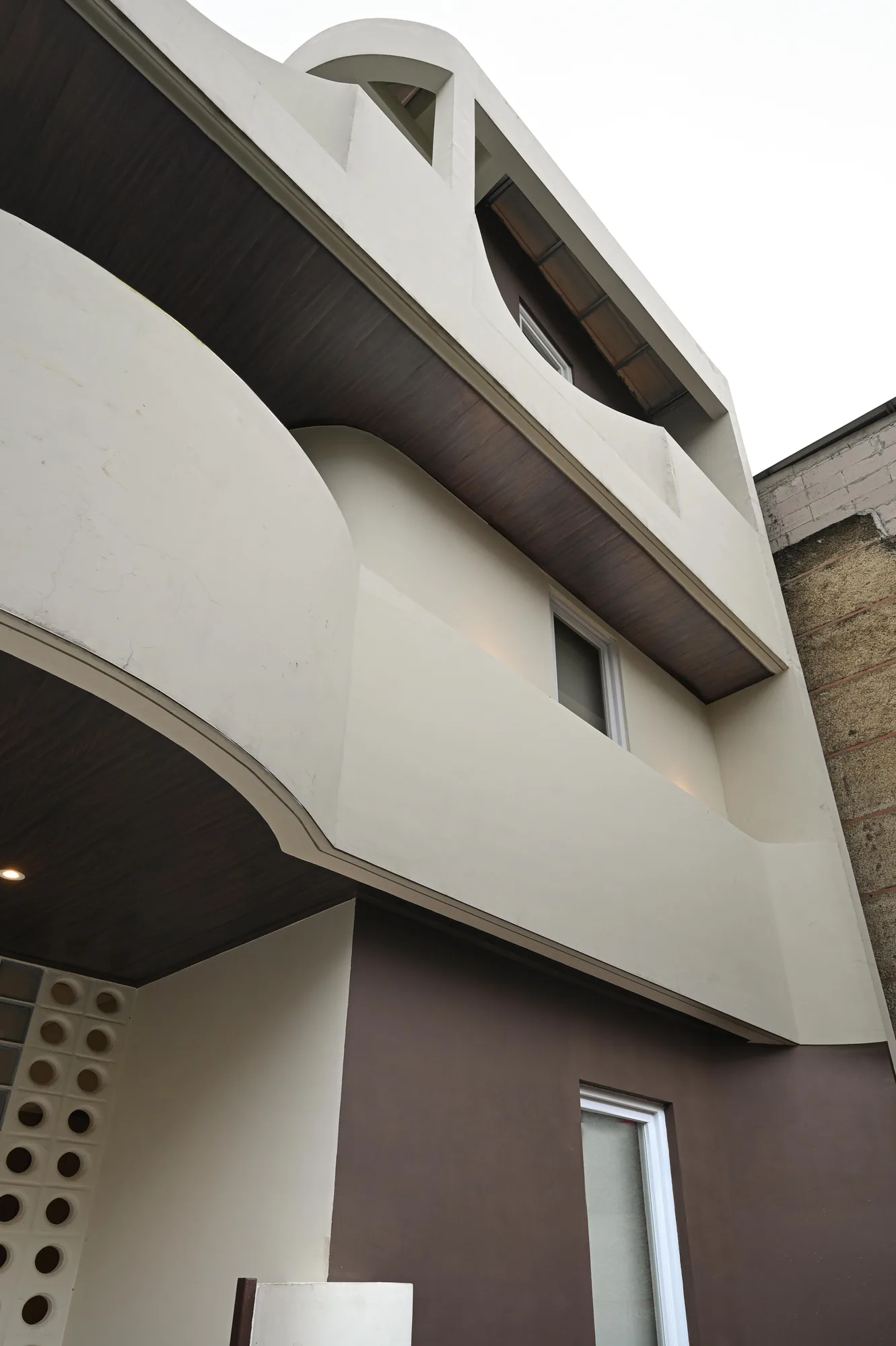 A steep upward view of the curved white facade, its balcony volumes stacked above the ground-floor entrance.