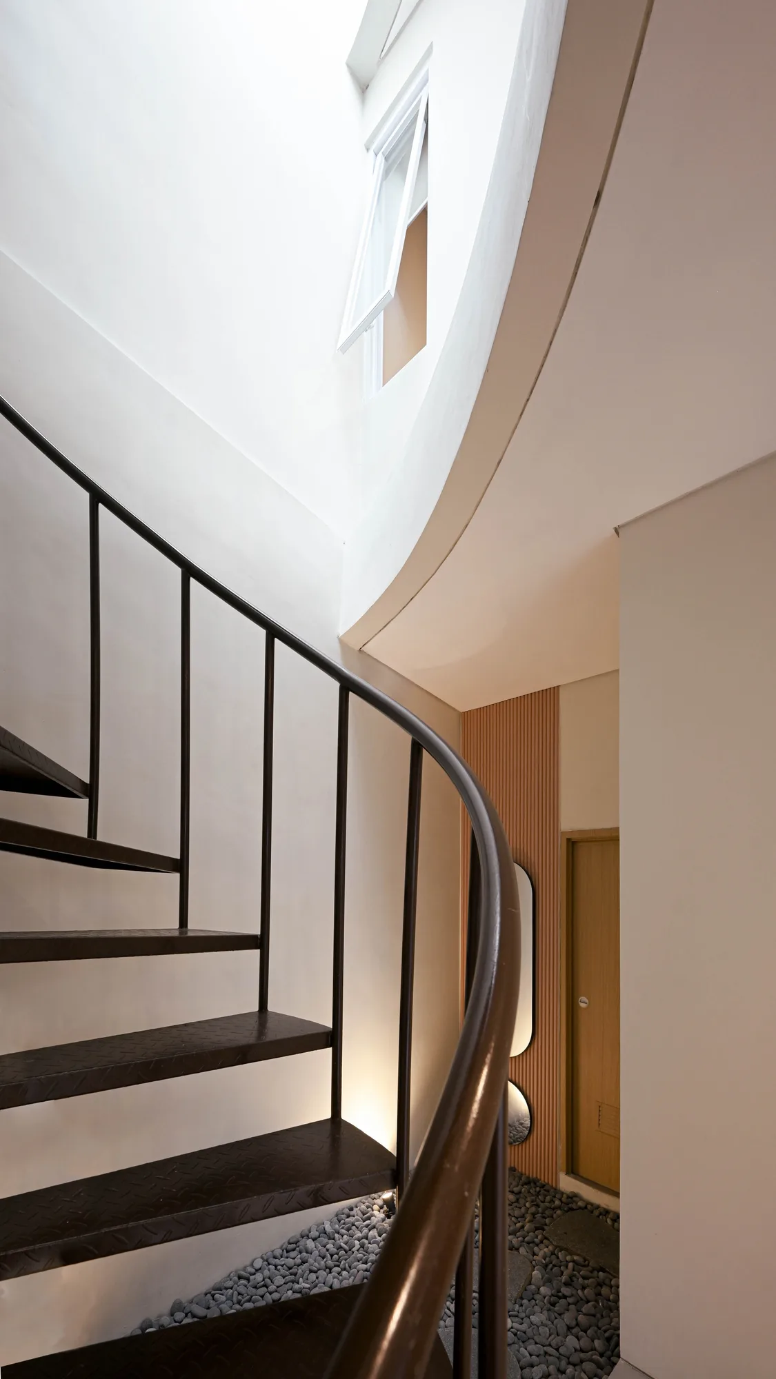 Looking up the spiral stair through the void, daylight falling from the window at the top past room 04's door below.