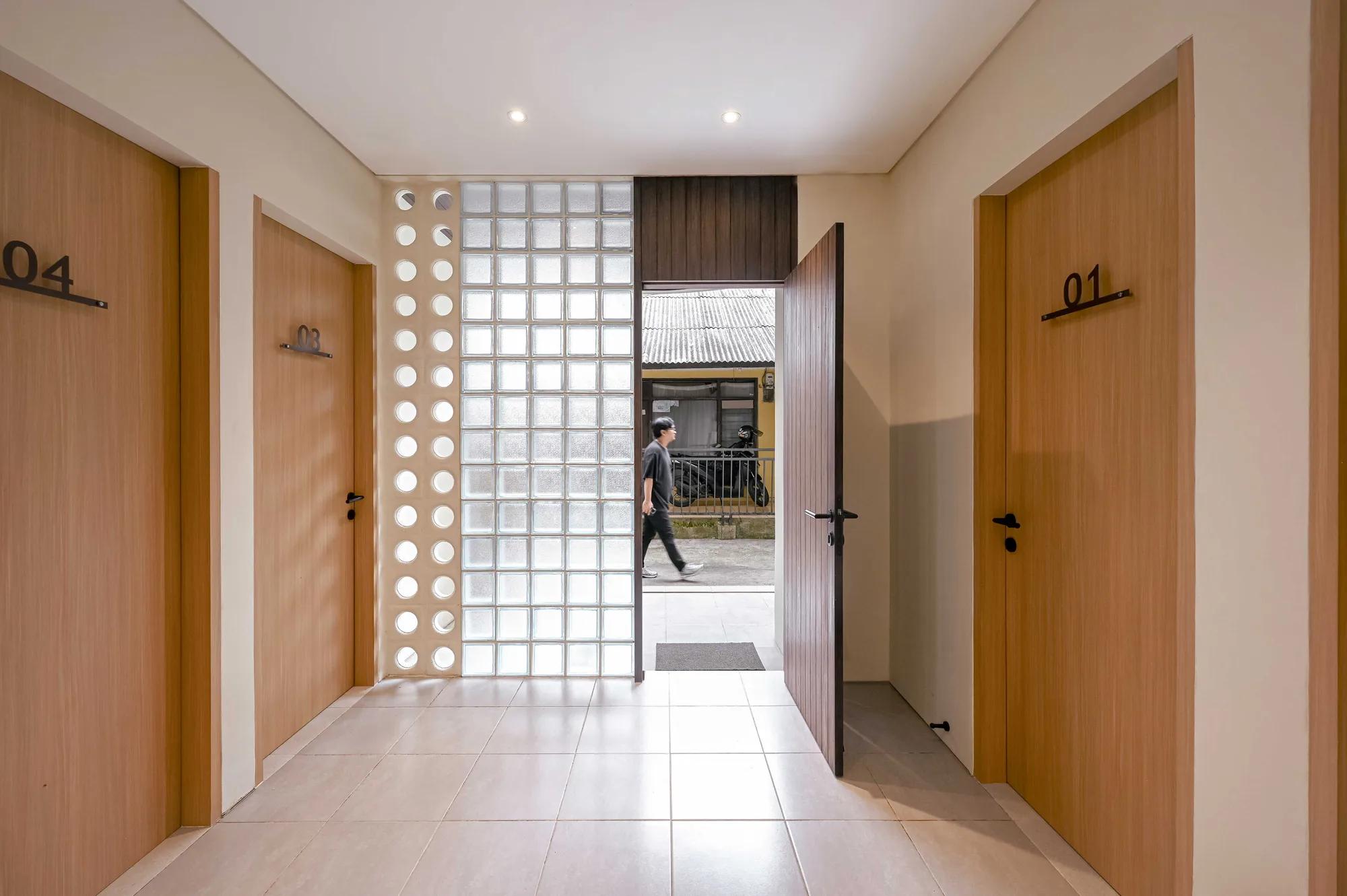 Ground-floor hallway framed by rooms 01 and 04, the front door open onto the street as a resident walks past outside.