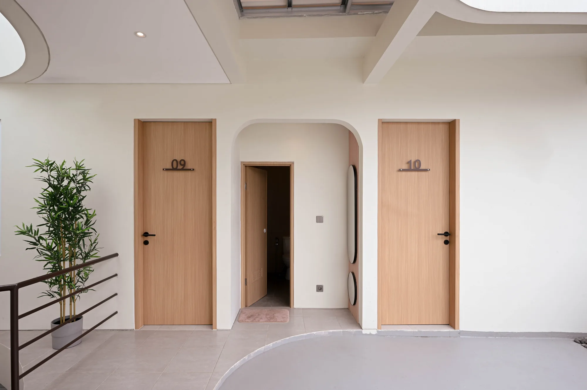 Upper-floor landing with a shared bathroom door ajar between rooms 09 and 10, a mirrored niche set into the curved wall.
