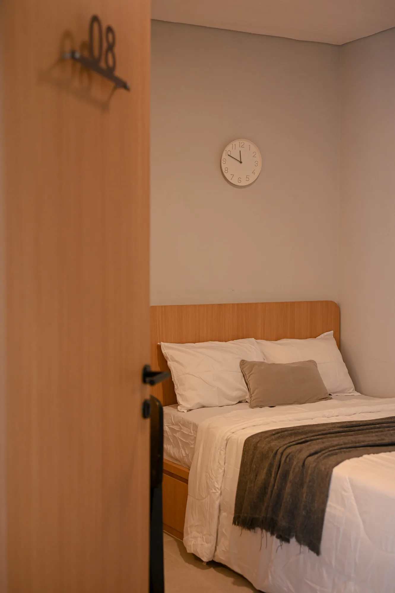 Room 08's door swings open onto the bed and wall clock inside, the room's warm palette softened by low light.
